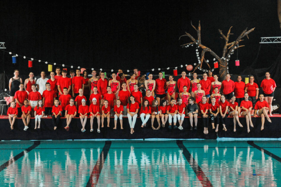 groupe de nageurs en tenues rouges posant au bord du bassin de natation