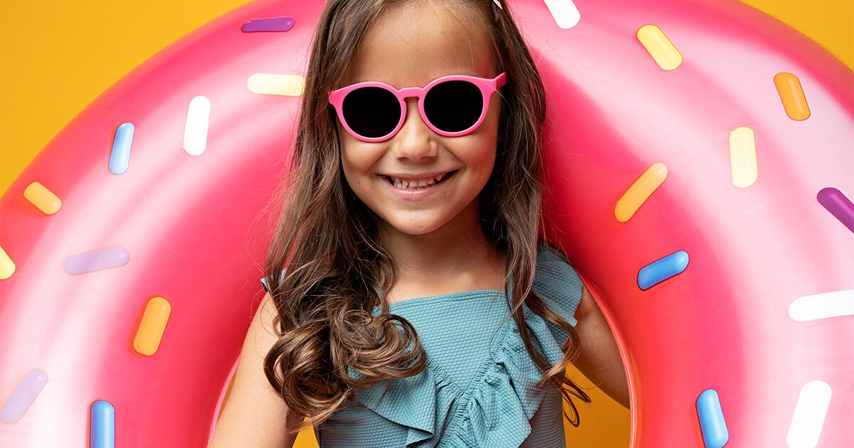 petite fille en lunettes de soleil tenant une bouée rose donut