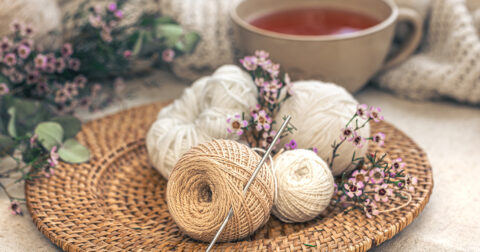 pelotes de tricot posées dans une assiette en rotin devant une tasse de thé