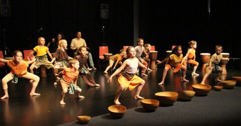 groupe d'enfants sur scène dansant au milieu de tambourins posés au sol