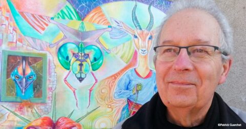 Homme aux cheveux courts gris et lunettes posant devant une peinture colorée représentant des animaux fantastiques