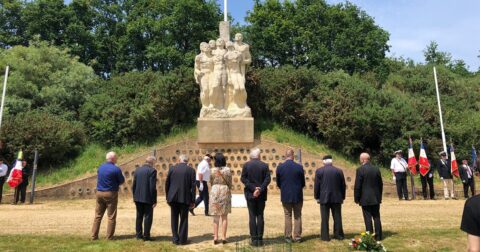 Anciens combattants de dos se recueillant devant une sculpture en extérieur