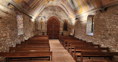 Intérieur d'une petite chapelle romane avec murs en pierre, banc en bois et nef peinte
