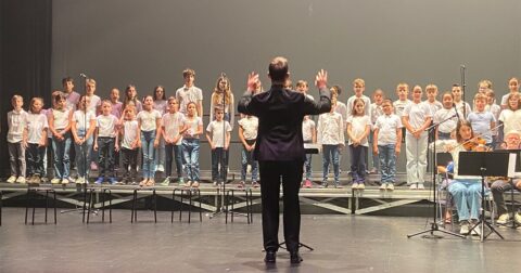 chorale d'enfants sur scène avec le chef de chœur