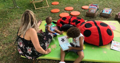 Maman avec ses deux enfants sur des tapis avec des livres assis dans l'herbe
