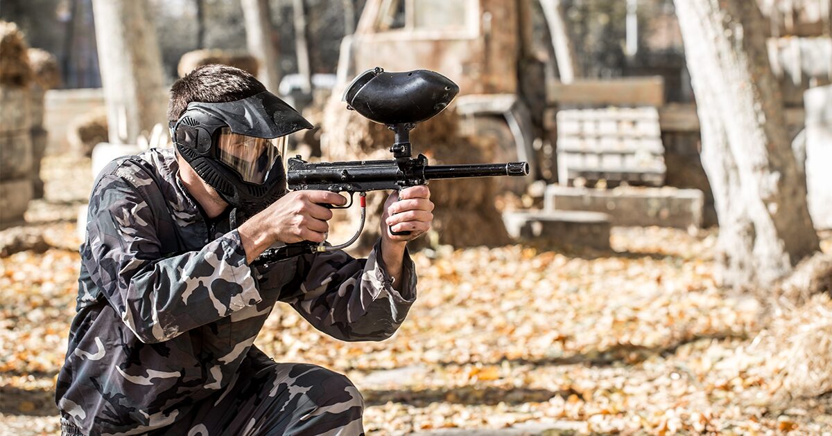 homme accroupi en tenue de camouflage avec casque et fusil de paintball