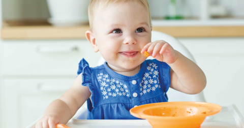 bébé assis dans une chaise haute souriant en mangeant son plat seul