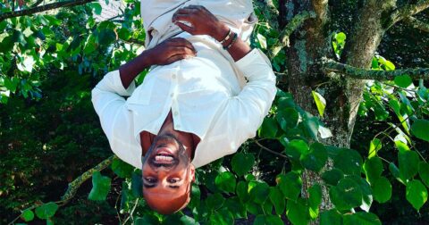homme habillé en blanc les jambes suspendues à un arbre