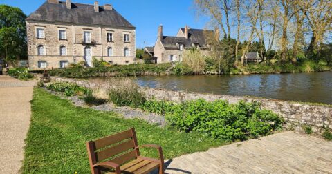 banc en bois au bord d'un étang avec vieille maison de maître en pierre en fond