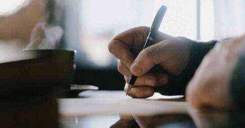 Une main écrivant avec un stylo argenté sur une feuille de papier.