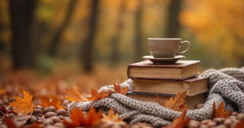 Couverture, livres et tasse empilés sur des feuilles mortes dans un bois