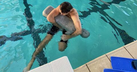 Un homme nageant avec un objet dans une piscine.