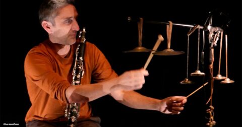 un musicien sur scène tape avec des baguettes sur des objets suspendus