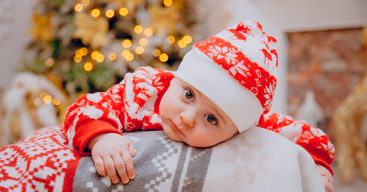 bébé avec pull et bonnet de Noël affalé sur le dossier d'un canapé