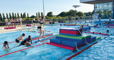 Nombreux enfants, ados et adultes s'amusant sur des tapis et obstacles dans une piscine extérieure